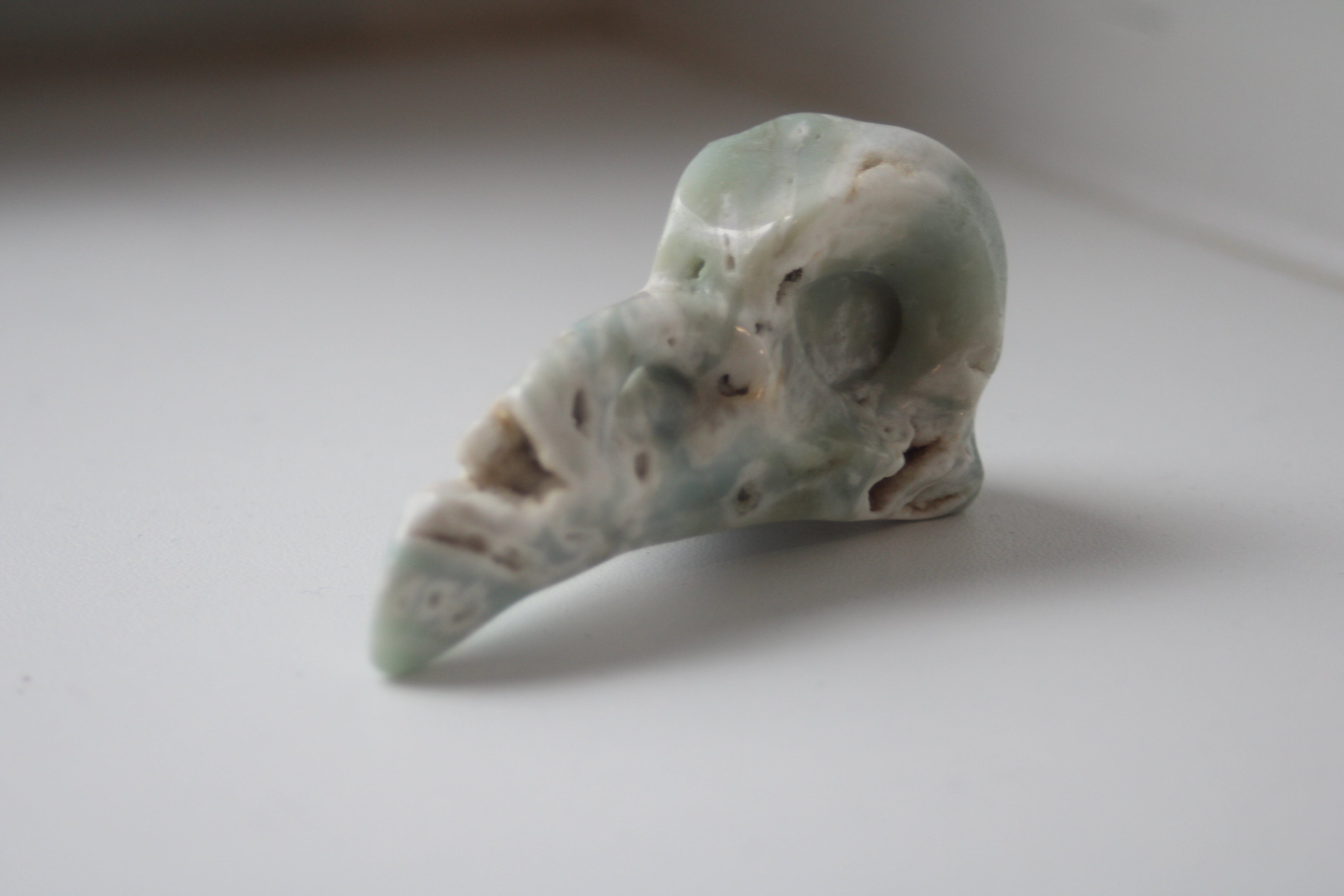 Voyagez aux confins de l'intuition avec ce crâne de corbeau en aragonite bleue, un gardien de sagesse qui diffuse une onde de sérénité absolue dans votre intérieur